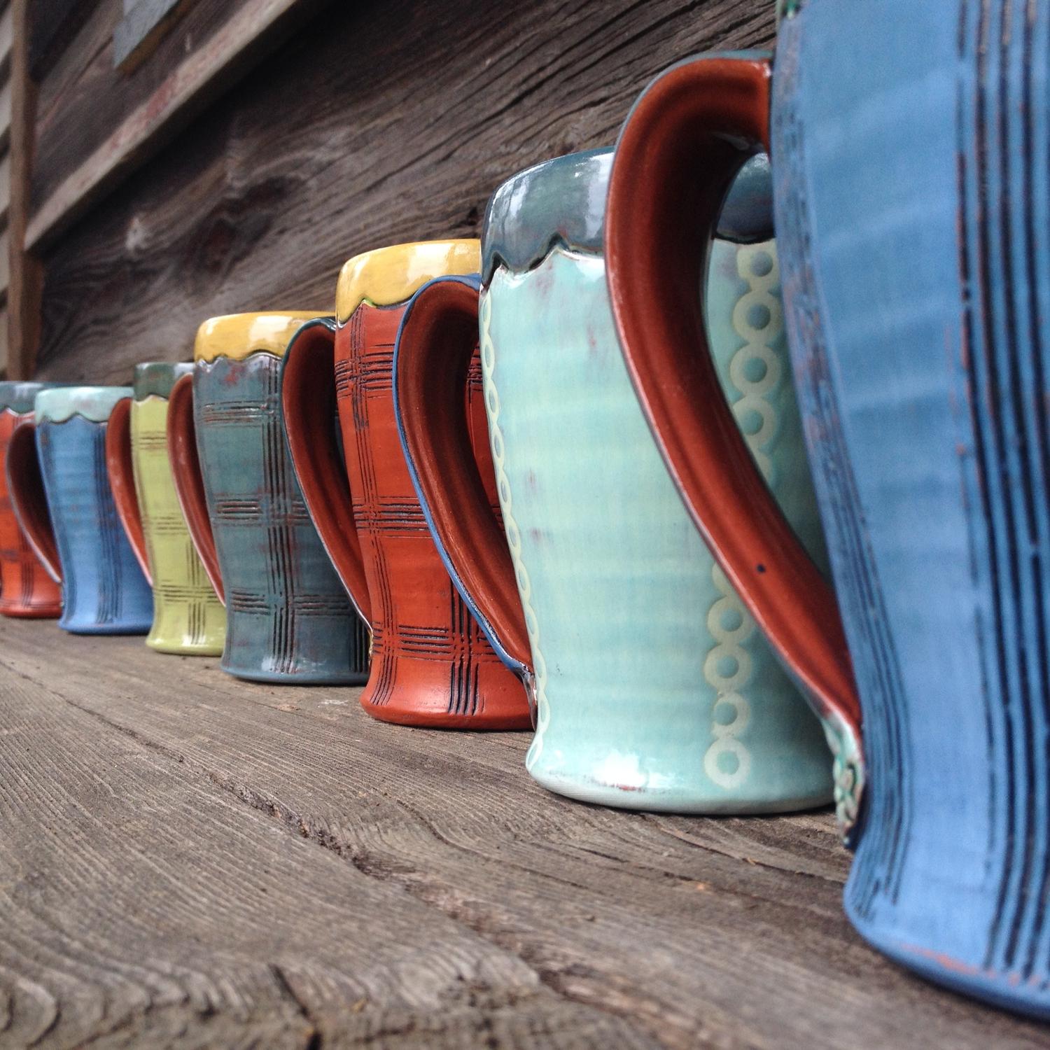 Row of vibrant colored ceramic coffee mugs created by artist 艾米·桑德斯.