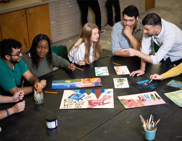 A studio classroom at Jacksonville University featuring students and a professor critiquing illustration work.