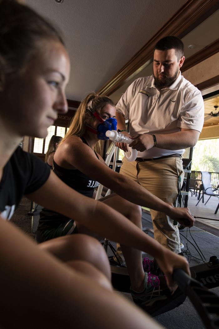 JU Rowing athlete participates in Exercise Science training simulation where she is rowing while an Exercise Science student monitors her vitals